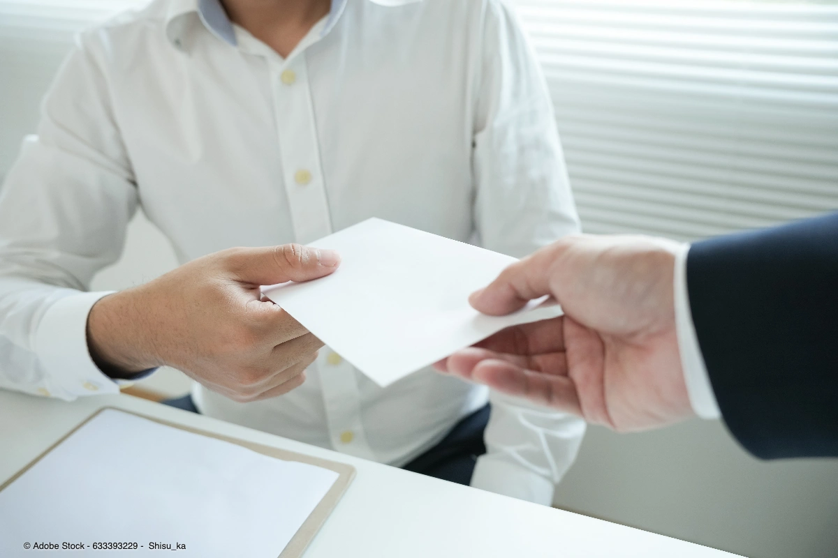 Zwei Personen überreichen einen Umschlag, passend zum Thema Mitarbeitergeschenke steuerlich absetzbar und deren korrekte betriebliche Dokumentation.